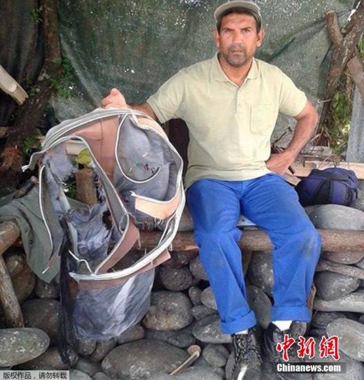 圖為當(dāng)?shù)貢r間7月30日，留尼旺島上的一名海岸清潔人員展示他找到的一個手提箱的殘骸。